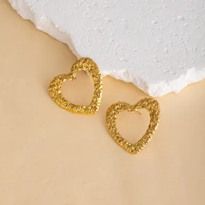 Close-up of textured gold heart earrings on a beige surface with white rock prop, detailed view.