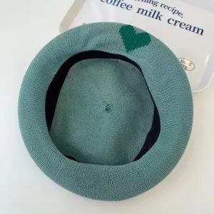 Close-up detail of green knitted mesh beret with dark green heart pattern for summer.