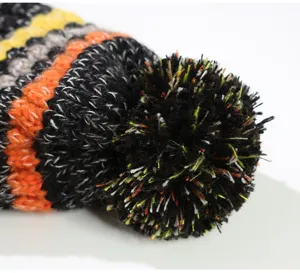 Close-up detail of winter warm knitted beanie hat with fluffy colorful pom-pom texture.