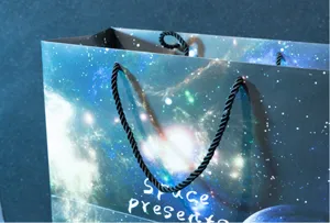Detailed view of galaxy print paper gift bag with sturdy black rope handles for presents.
