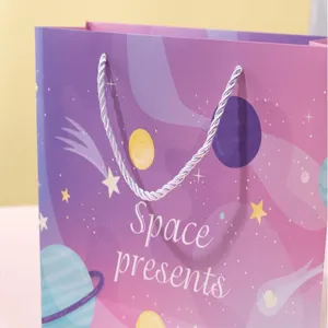 Detail view of pink galaxy paper gift bag with white rope handles and space star patterns.