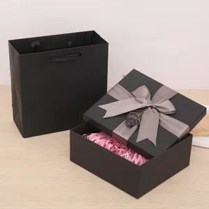 Black gift box and matching bag set with grey ribbon bow and pink shredded paper inside.