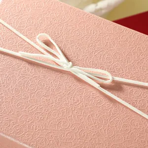 Close-up detail of elegant pink textured gift box adorned with a delicate white ribbon bow.