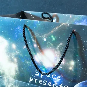 Starry night galaxy gift paper bag with black rope handles for presents and holiday packaging.