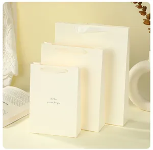 Elegant beige paper gift bags with white ribbon handles, perfect for various presents.
