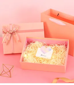 Pink gift box set with ribbon bow, paper bag, shredded paper and fairy lights for birthday.