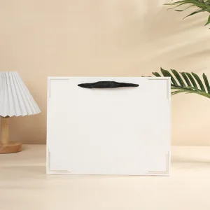 Witte papieren geschenktas met zwart lint handvat en elegante gouden rand voor stijlvolle kadoverpakking.