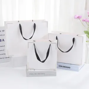 White paper gift bags set with black ribbon handles and elegant gold corner designs for festive gifting.