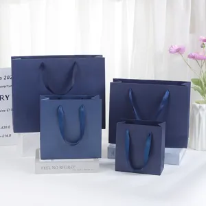 Dark blue paper gift bags detail view, elegant ribbon handles for cosmetic and festival packaging.