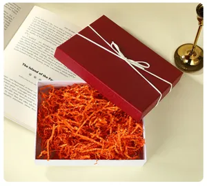 Detail shot of a red gift box with white ribbon and orange shredded paper filler.
