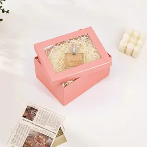 Vista detallada de la caja de regalo rosa con ventana, rellena de papel y frasco de perfume.