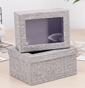 Detalle de caja de regalo de tela gris, tapa con ventana transparente para cosméticos.