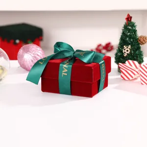 Red velvet gift box detail, dark green ribbon bow with gold letters, premium holiday packaging.