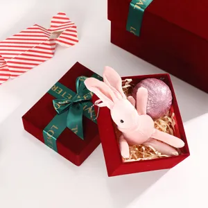 Wine red velvet gift box detail featuring green ribbon bow and cute pink plush rabbit toy inside.