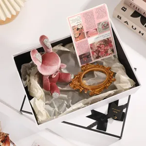 Close-up detail view of white gift box with pink plush bunny toy, ribbon tag, and aesthetic props.
