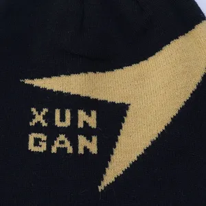 Close-up detail of black knitted beanie hat with stylish yellow jacquard letter graphic design.