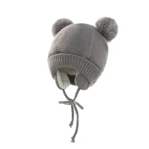 Detailaufnahme einer grauen Kinderstrickmütze mit Bommeln, Ohrenklappen und Plüschfutter.