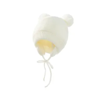 Nahaufnahme der süßen weißen Kinder-Strickmütze mit zwei Bommeln und praktischen Ohrenklappen.