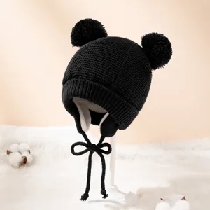 Schwarze Kinder Strickmütze Detail mit flauschigen Pompons und warmem Plüschfutter.