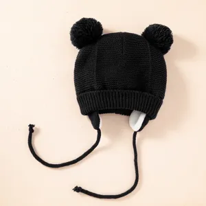Detailansicht der schwarzen Strickmuetze mit niedlichen Pompons, Ohrenklappen und Baendern.