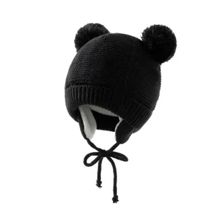 Nahaufnahme der schwarzen Strickmütze mit doppelten Pompons, Ohrklappen und Kinnbändern.