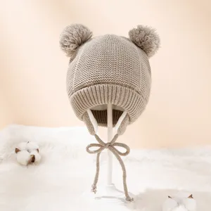 Detailansicht der niedlichen Kinder Strickmütze mit Doppelpompons und Ohrklappen in Beige.