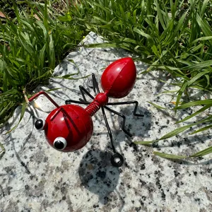 Close up of red metal ant figurine, iron insect garden decor on stone background outdoors.