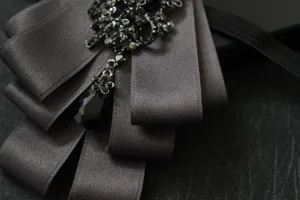 Detailed close-up of multi-layer fabric bow tie with black rhinestones and crystal drop.