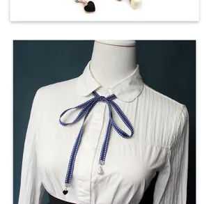 Detailed shot of a navy blue polka dot ribbon tie with heart and pearl charms on shirt.