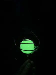 Gros plan d'un pendentif carillon éolien lumineux brillant en vert dans le noir avec support.