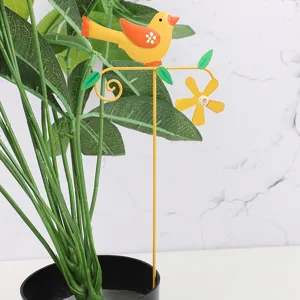 Detail shot of a cute yellow metal bird garden stake inserted into a green potted plant decor.