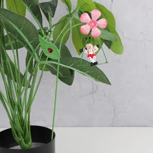 Detail view of metal garden stake, cute swinging figure and pink flower on potted plant