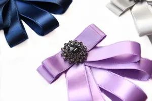 Exquisite satin ribbon bow brooch with crystal rhinestone center detail, perfect for suits.