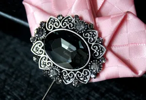 Detailed close-up of vintage black crystal oval brooch with silver filigree on pink ribbon.