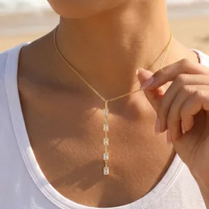Nahaufnahme einer zarten Goldkette mit einem vertikalen Anhänger aus funkelnden Steinen.