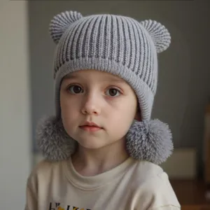 Close-up detail of grey knitted baby hat featuring cute bear ears and fluffy pom-pom earflaps.