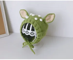 Detailansicht einer bezaubernden grünen Baby-Strickhaube mit verspielten Hirschohren und Bommeln.