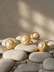 Detailed close-up of textured gold-plated pearl rings displayed elegantly on smooth pebbles.