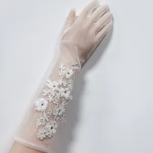 Vista dettagliata di lunghi guanti da sposa bianchi in tulle con ricamo floreale in pizzo e perle.