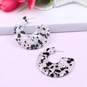 Detailed view of C-shape clear acrylic earrings with black and white stone confetti inside.