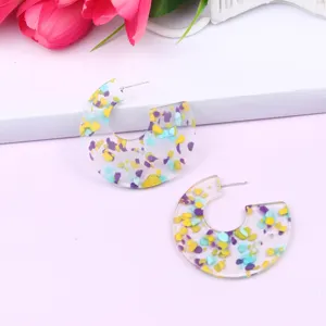 Close-up detail of C-shaped transparent acrylic earrings filled with colorful gemstone glitter.