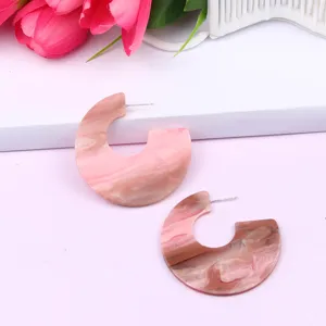 Close-up of C-shaped pink acrylic marble texture earrings, simple geometric jewelry.