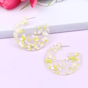 Detailed close-up of C-shaped acrylic earrings with yellow and white glitter flakes inside.