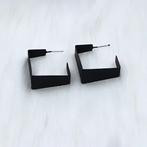 Close-up detail of modern black geometric open hoop earrings on white fluffy fur background.