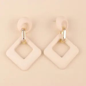 Primer plano detallado de pendientes geométricos de acrílico beige con anillos de metal.