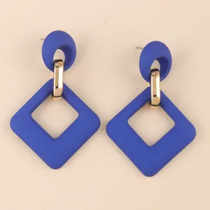 Primer plano de pendientes geométricos azules de acrílico con eslabones dorados, detalle de joya.
