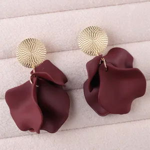 Close-up detail of stylish dark red petal earrings with textured gold discs on velvet.