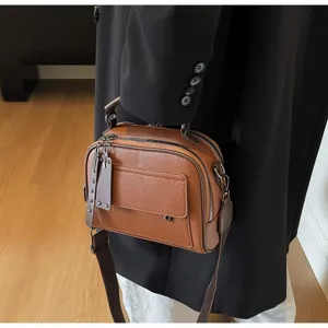 Nahaufnahme einer braunen Schultertasche aus weichem Leder mit Reißverschluss und Vordertasche.