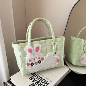 Hellgrüne geflochtene Handtasche mit Plüschhasen-Aufnäher, ideal für Strand und Alltag.