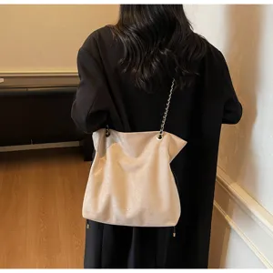 Detail shot of the beige suede drawstring tote bag showcasing its metal chain strap and soft body.
